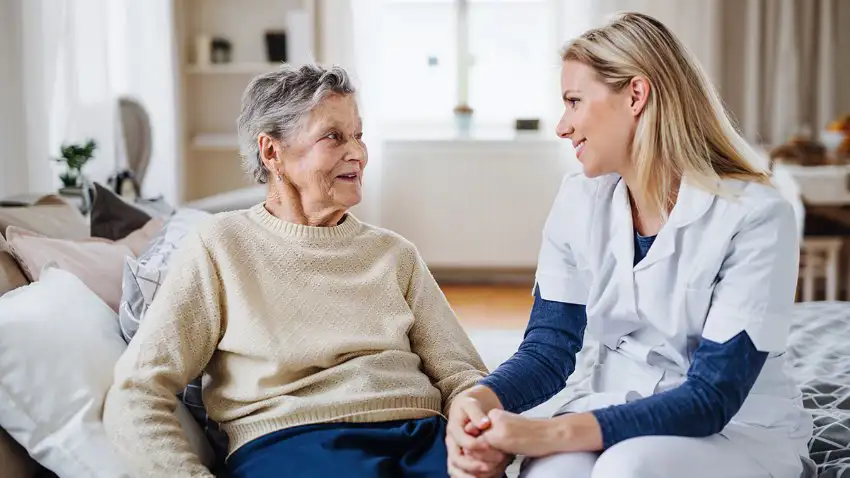 Female caregiver holding an elderly female patient's hand.