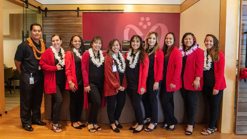 Group of 10 professionally dressed people wearing Hawaiian leis standing in a row in a building lobby.
